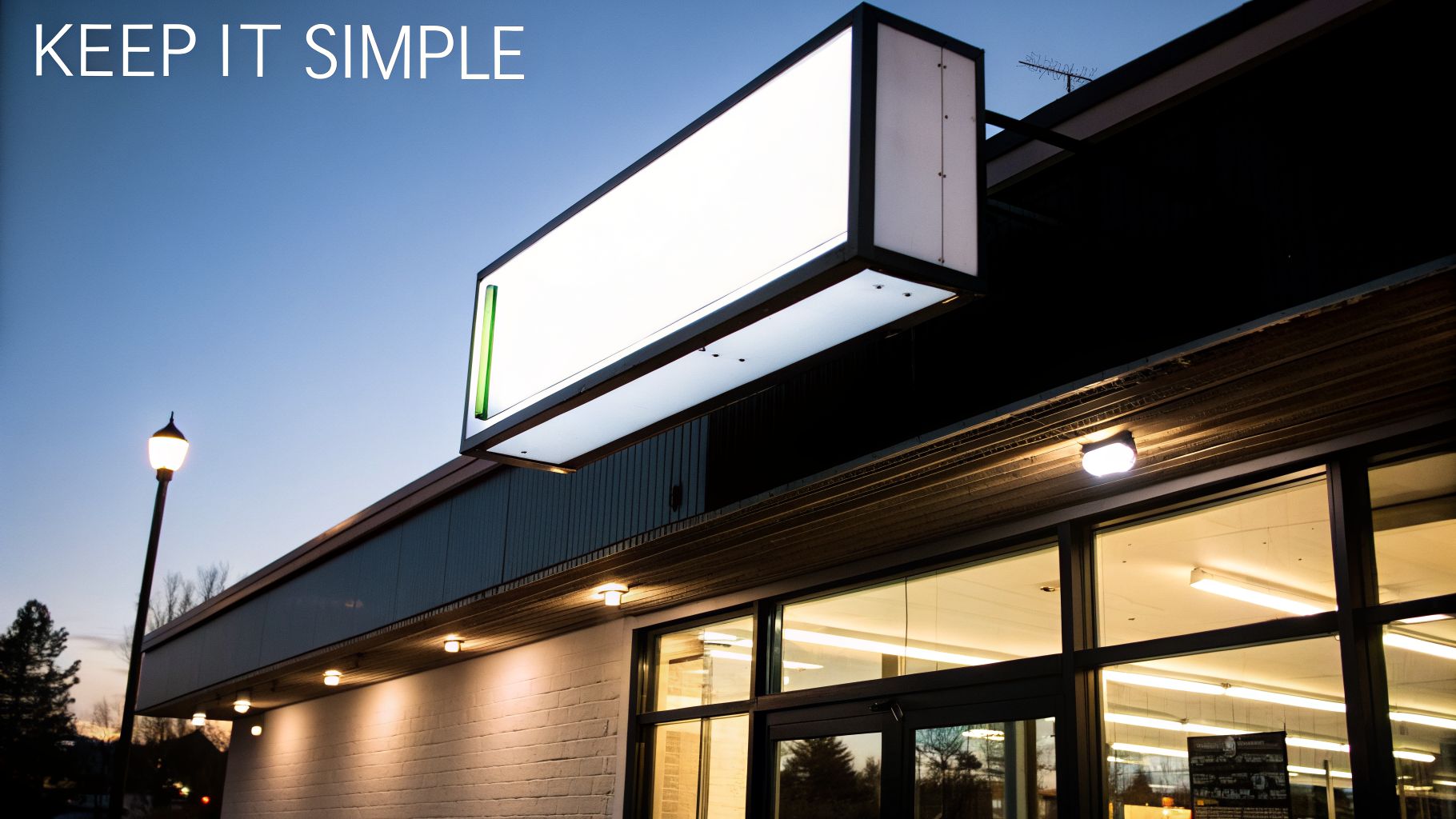 An illuminated rectangular lightbox sign hangs over a modern building with large windows at dusk.